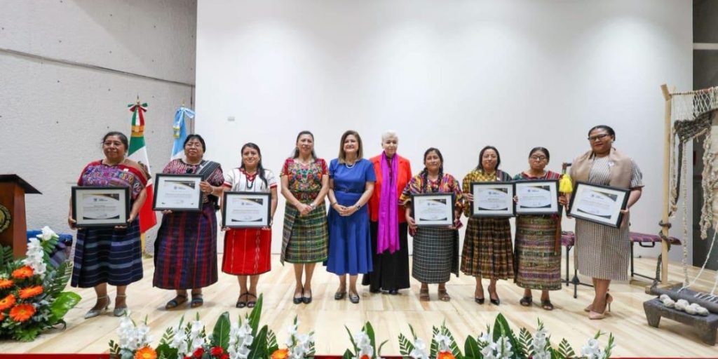 Siete mujeres indígenas distinguidas con la Orden Ütz Samaj sosteniendo sus diplomas y condecoraciones durante la ceremonia oficial.